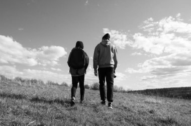 Çimenli bir tepede sırt çantalı iki kişinin kameradan uzaklaşırken çekilmiş siyah beyaz bir fotoğrafı. Gökyüzü kabarık bulutlarla aydınlık..
