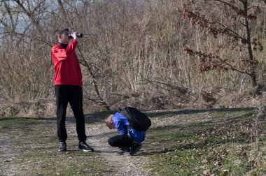 Kırmızı kazaklı bir çocuk su şişesinden içerken diğer çocuk eğilip muhtemelen sırt çantasını tamir ediyor. Onlar ender ağaçların arasında bir yoldadırlar..