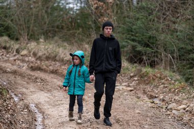 Genç bir çocuk, küçük kız kardeşiyle el ele yürür. Doğanın güzellikleriyle çevrili, yapraklarla kaplı bir patikada. Serin hava, sakin ortamı doldurur..
