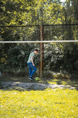 Genç bir insan çimenli bir arazide tel örgülerin yanında ustalıkla bir futbol topuyla hokkabazlık yapıyor. Ayarlar bir park ya da eğlence alanı gibi görünüyor..
