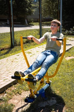 Genç bir insan spor yaparken açık hava spor aletlerini kullanır. Sahne parlak ve güneşli, açık havada sağlıklı bir aktivite sergiliyor..