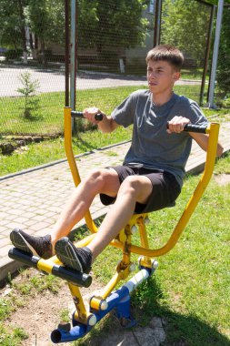 Genç bir adam bir park ortamında açık hava idman ekipmanı kullanıyor. Egzersizine odaklanmış, dışarıda sağlıklı aktiviteler sergiliyor..