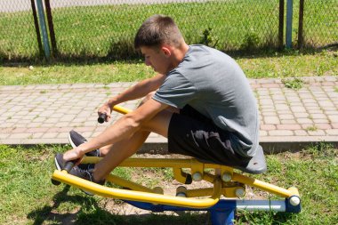 Genç bir adam spor yapmaya odaklanır, açık hava spor malzemelerini kullanır. Oturdu ve kollarını çekti. Gücünü ve kondisyonunu gösteriyor..