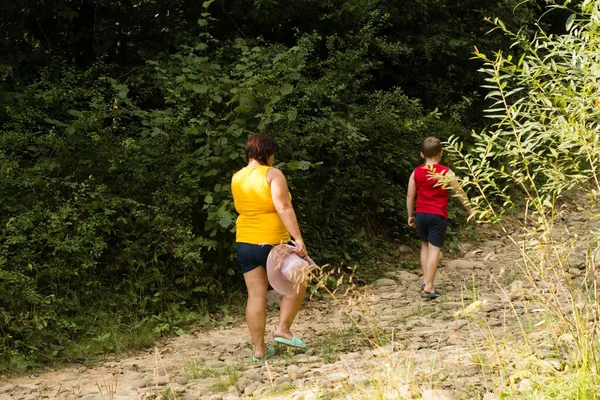 Bir kadın ve bir çocuk ormanda bir patikada yürüyüş yapıyorlar. Kadın bir şapka taşıyor ve kameradan uzaklaşıyorlar..
