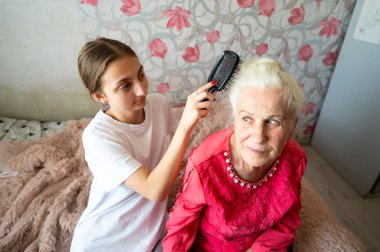 Çiçeklerle süslenmiş sıcak, rahat bir yatak odasında, genç bir kız nazikçe büyükannesinin saçlarını tarıyor, nesilleri aşan bir sevgi ve bağlantı anı yaratıyor..