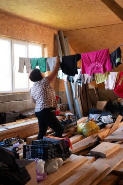 Ahşap panelli duvarları ve tavanı olan bir odada bir kadın çamaşırlarını ipe asıyor. Kereste ve çeşitli kutular zemini darmadağın ederek evcillik hissi yaratıyor. Sahne basit ve gerçek..