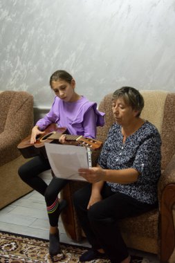 Bir kız, müziğe bakan bir kadın tarafından yardım edilirken gitar çalmayı ve nota okumayı öğreniyor. Sahne kapalı, rahat ve rahat bir yerde çekiliyor..