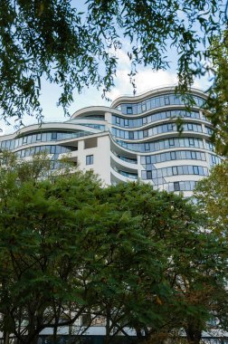 Modern binaların ince çizgileri ve kıvrımları yemyeşil yeşilliğin üzerine yükseliyor, mimari ve doğanın parlak mavi gökyüzüne karşı uyumlu bir karışımını sergiliyor..