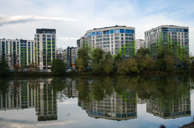 Çağdaş apartman kompleksleri canlı renkler sergilerken yansımaları yemyeşil yemyeşil gölün sakin yüzeyinde dalgalanır..