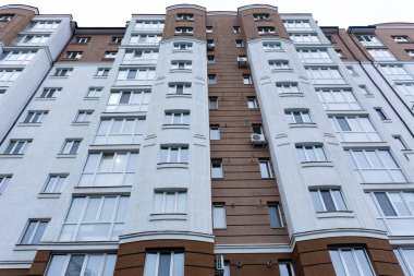 Büyük şehir yapısı akşam gökyüzüne yükselir, kahverengi ve beyaz renkli canlı bir cephe içerir. Pencereler alacakaranlığın yumuşak parıltısını yansıtıyor, mimari zarafeti arttırıyor..