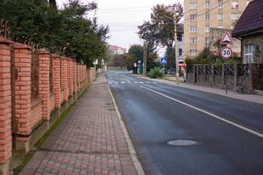 Sabahın erken saatlerinde, tuğla duvarlarla çevrili ağaçlarla kaplı bir sokakta huzur dolu bir parıltı salıyor. Sakin bir mahallede gün doğarken sükuneti davet ediyor..