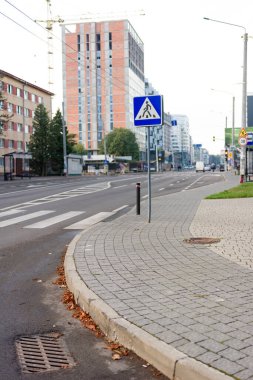 Sabah ışığı boş bir şehir caddesini aydınlatıyor, yaya geçidi tabelasının kaldırım kenarında nöbet tuttuğu, çağdaş mimariyle çevrili..