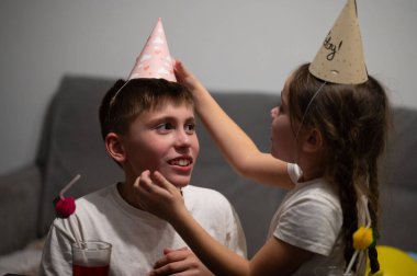 Parlak tebessümler odayı aydınlatırken bir kız arkadaşının kafasına bir doğum günü şapkası takıyor, öğle vakti etrafı abur cubur ve neşe dolu dekorasyonlarla çevrili..