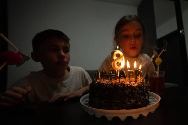 Genç bir kızın çikolatalı doğum günü pastasına mum üflemek için öne doğru eğildiği, sönük bir odada heyecan ve sıcaklıkla çevrili neşeli bir toplantı gerçekleşiyor..