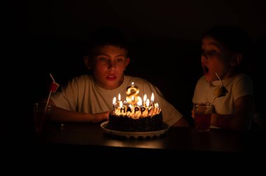 İki erkek çocuk, güzel dekore edilmiş mumlarla süslenmiş, saf heyecanı yansıtan bir pastaya odaklanmış, yürek ısıtan bir doğum günü kutlamasıyla meşgul..