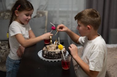 İki çocuk renkli malzemelerle bir pastayı süslemeye çalışır. Sıcak bir odada gülücükler ve kahkahalar paylaşırlar..