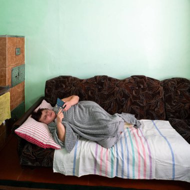 Bir insan rahat bir kanepede, yumuşak bir battaniye giyerken akıllı telefonuyla dinlenir. Huzurlu ortam uzayın sakin atmosferine katkı sağlar..