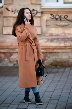 Şık bir genç kadın kaldırım taşı bir sokakta duruyor, bir telefon görüşmesi yapıyor, şık dış giyim ve botlarına güveniyor, kentsel sanat eserleriyle çevrili..