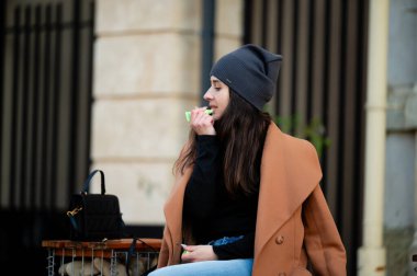 Büyüleyici bir şehir ortamında oturan genç bir kadın, sıcacık giyinmiş, gevşek bir tavırla atıştırmasından bir ısırık alıyor, rahatlık ve rahatlığın mükemmel bir karışımını somutlaştırıyor..