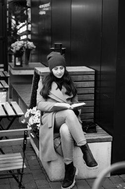 Yumuşak bir günbatımının altında, genç bir kadın rahat bir şekilde bir bankta oturur, kitabına dalmış, çiçek açan ve huzurlu şehir titreşimleriyle çevrili..