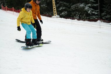 İki snowboardcu, kışın tadını çıkarırken arka planda ağaçlarla dolu bir yamaçta, gülücüklerini ve heyecanlarını paylaşıyorlar..