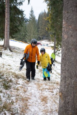 Yetişkinler ve çocuklar karlı bir yolu keşfederken snowboard sporunun eğlenceli bir gününe hazırlanıyorlar. Etrafı hep yeşil ağaçlarla çevrili ve kış cazibesiyle huzurlu bir dağ ortamında..