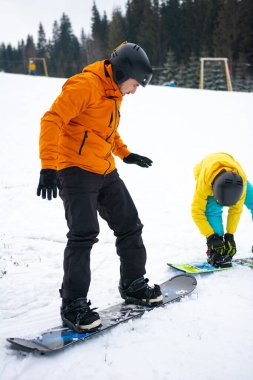 İki tutkulu snowboardcu, karlı bir yamaçta etrafları hep yeşil ağaçlarla çevrili kış güneşinde taze toz oymak için heyecanlı bir güne hazırlar..