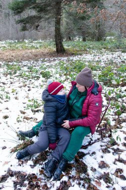 Karla kaplı bir ormanda bir kızağın üzerinde yuvalanmış bir ebeveyn ve çocuğun yürek ısıtan bir sahnesi. Çocuk, ailesine sevgiyle bakar ve dokunaklı bir kış anı yaratır..