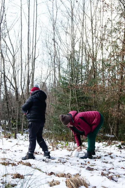 İki genç, ormanda karlı bir günün tadını çıkarıyor. Küçük bir kardan adam yapıyorlar. Kış manzarası sakin, çıplak ağaçlar ve zemini kaplayan hafif bir kar tozu..