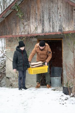 Bir adam ve bir çocuk, karlı bir kış ortamında kırsal bir binanın yakınında bir sepet odun taşıyorlar. Birlikte çalışırlar, aile işlerini ve kış işlerini gösterirler..