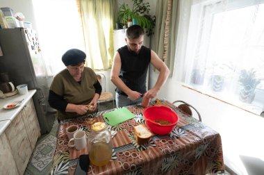 Güneş ışığıyla dolu sıcacık bir mutfakta, yaşlı bir kadın, genç bir adama yemek pişirme becerilerini öğretir. Malzemeleri keserken, bir anlık bağlantının ve kahkahanın tadını çıkarırlar..