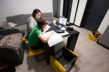 Öğrenci masaya odaklanmış, online derslere aktif olarak katılıyor. Bakıcı, sıcak ve davetkar bir yerde besleyici ve üretken bir atmosfer sağlar..