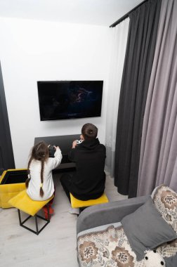 İki kardeş heyecanlı bir oyun seansına katılır, sıcak dekore edilmiş oturma odasındaki sarı taburelerde otururlar, büyüleyici bir deneyim için ışıklar kararır..