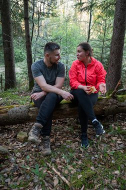 Huzurlu bir orman ortamında, bir çift bir kütüğe oturur, uzun ağaçların arasından süzülen canlı yeşillikler ve yumuşak güneş ışığıyla çevrili sohbet ve kahkahalarla meşgul olurlar..