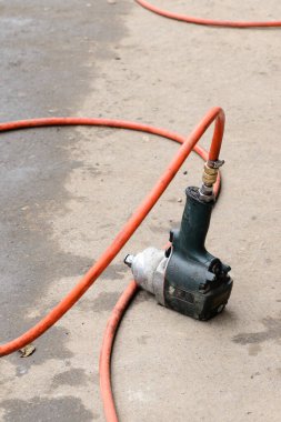 Bir elektrikli hava pompası, kırmızı bir hortumla beton zeminde duruyor. Sahne, çeşitli görevler için araçların kullanıldığı bir garajda ayarlandı.