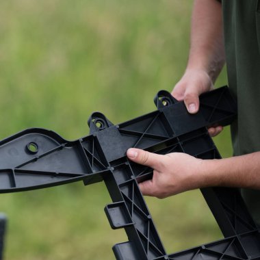 Karmaşık, siyah plastik bir parçayı tutan ellerin yakın çekimi. Karmaşık tasarım ve doku bulanık yeşil bir arkaplan karşısında belirgindir..