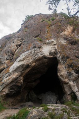 Dağlardaki büyük gri taşlardan yapılmış karanlık mağara girişi - fotoğraf