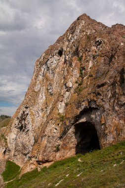 Dağlardaki büyük gri taşlardan yapılmış karanlık mağara girişi - fotoğraf