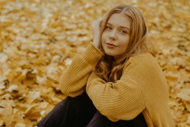 Sonbaharda, sonbahar yapraklarının arka planında parkta güzel bir kız kameraya bakar..