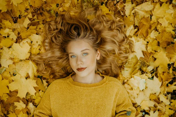 美しい少女は秋に公園にいます オレンジの葉を背景に黄色いセーターを着た10代 ブロンドはカメラを見ている ファッションとスタイル — ストック写真