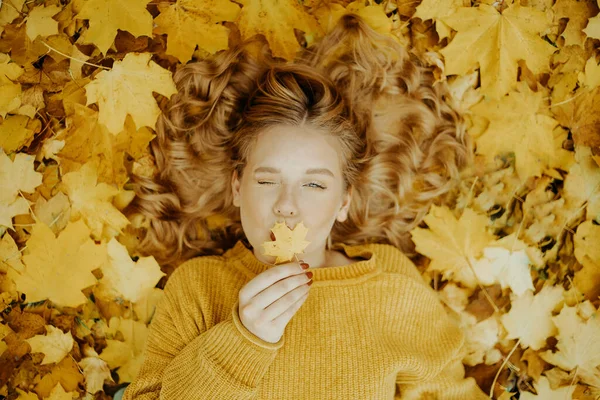 美しい少女は秋に公園にいます オレンジの葉を背景に黄色いセーターを着た10代 ブロンドは笑顔で笑う ファッションとスタイル キスを吹く女 — ストック写真