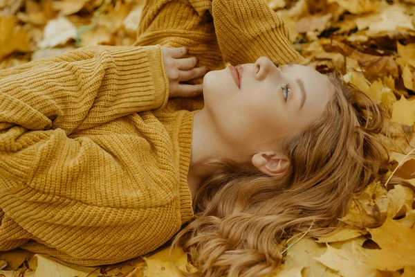 美しい少女は秋に公園にいます オレンジの葉を背景に黄色いセーターを着た10代 ブロンドは笑顔で笑う ファッションとスタイル 休む女 — ストック写真