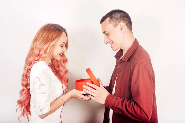 白い背景に恋人のペア 男は女性に新年の贈り物を与える クリスマス 男は箱を手にして女の子は微笑む — ストック写真