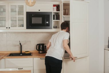 Bir adam mutfakta durur ve buzdolabına bakar, ne yiyeceğini bilmez, akşam yemeği, kahvaltı, öğle yemeği için ne pişireceğini düşünür. Bekar adam yemek yapıyor. Sağlıklı yiyecekler, düzgün beslenme. Yemek teslimatı