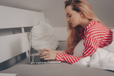 Kız dizüstü bilgisayarla yatakta yatıyor. Evden çalışmak, tembellik. Kız internette bir şeyler yazıyor, serbest çalışıyor..
