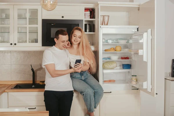 A woman and a man order food online. A couple is standing in the kitchen near the refrigerator and buying food through the phone. Online shopping, delivery.