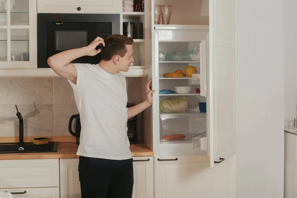 Man Stands Kitchen Looks Refrigerator Does Know What Eat Thinks — Stock Photo, Image