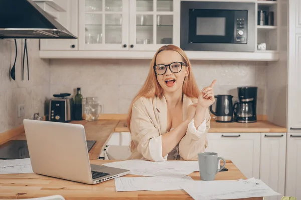 Woman at laptop works from home, student, teacher. A beautiful blonde in a jacket and glasses looks at the camera, the girl came up with the idea of earning money online.