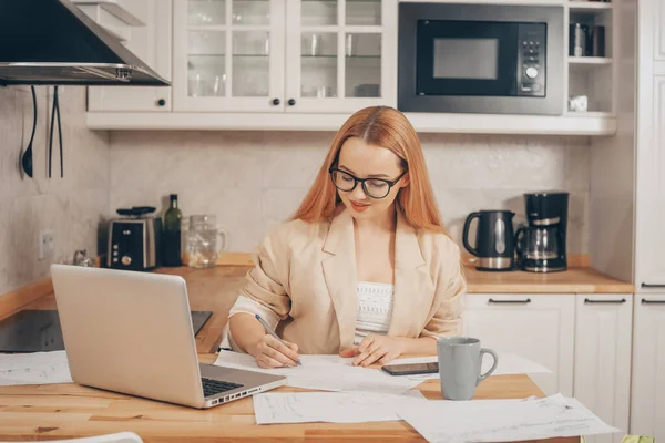 Woman at laptop works from home, student, teacher. A beautiful blonde in a jacket and glasses looks into a laptop and writes something down. Online training, work freelance accountant.