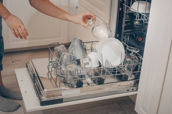 Built-in dishwasher, dishwashing. A woman loads washed dishes, cups, glasses. A woman\'s tender hand puts a glass goblet in the dishwasher or pulls out, unloads.